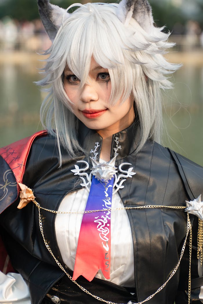 Fantasy cosplayer with white hair and animal ears in an elaborate costume posing outdoors.