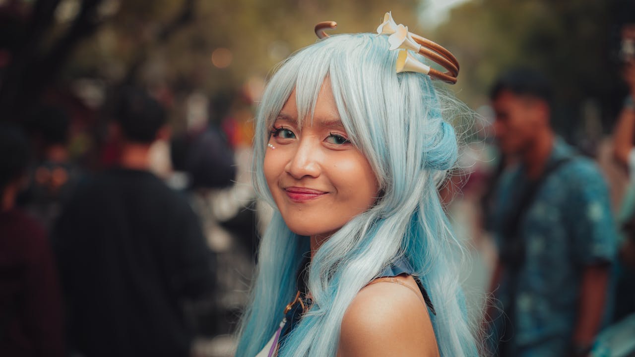 A woman in blue cosplay attire smiles at an outdoor event.